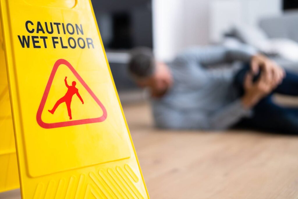 Photo of a Man Holding a Knee Next To Wet Floor Sign