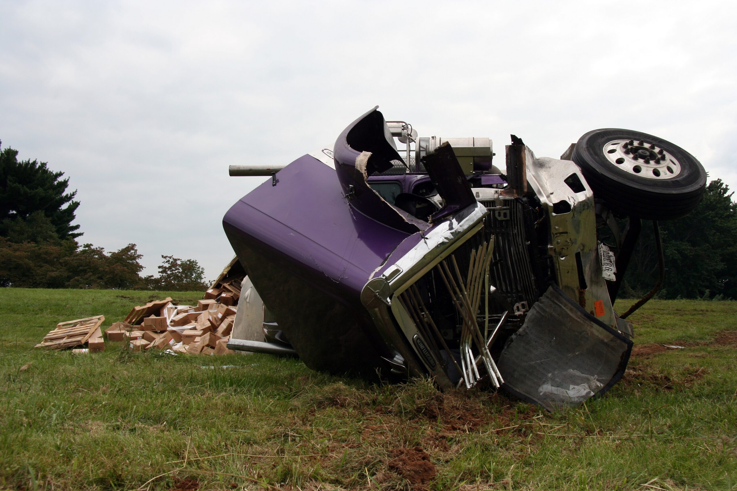 Purple truck with a crushed front end, flipped over in crash with cargo spilling out