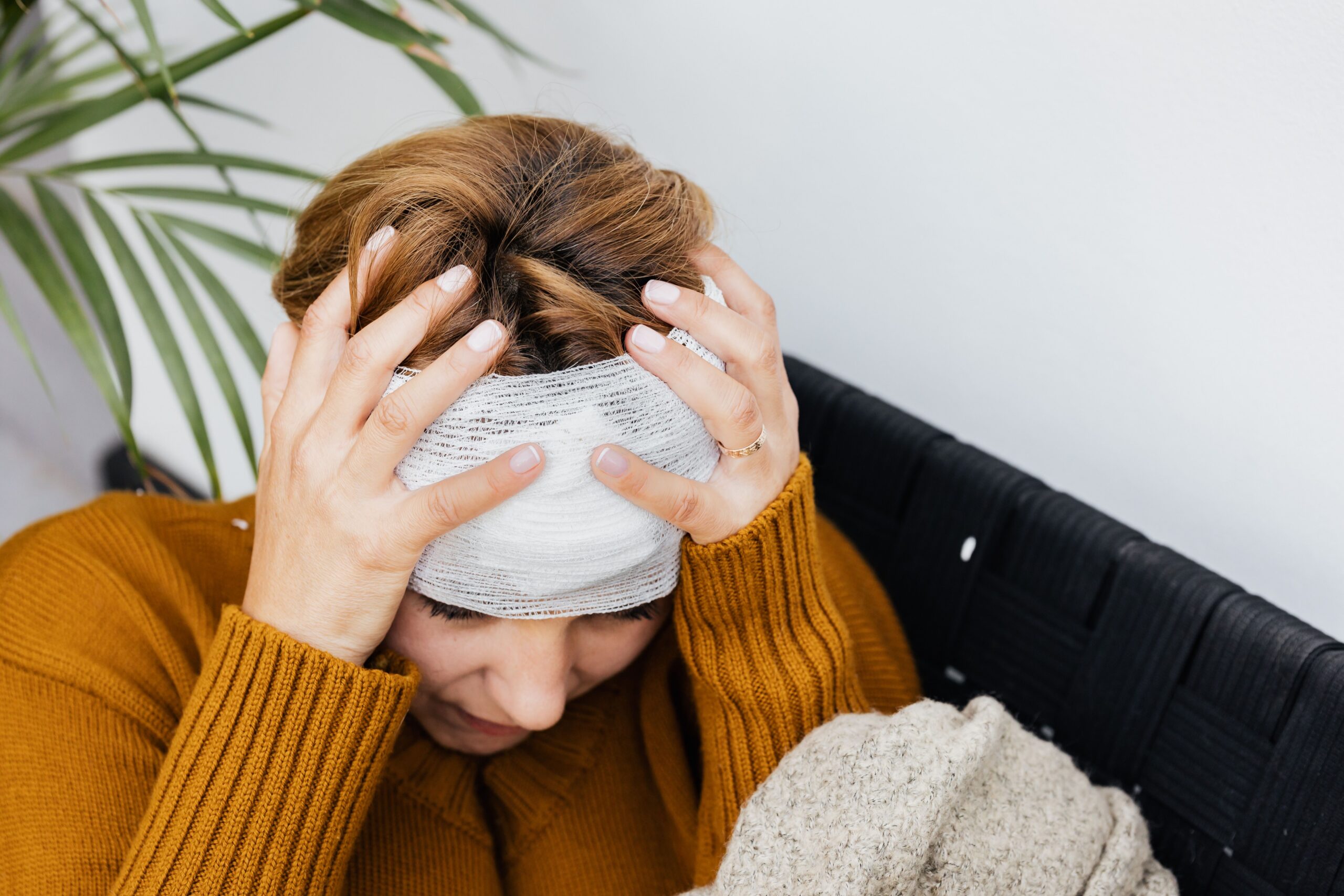 Person with bandaged head holding head in hands while sitting on a couch